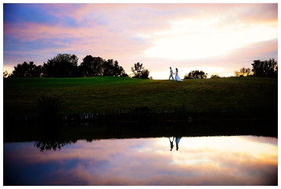 bride and groom at sunset with reflection in pond