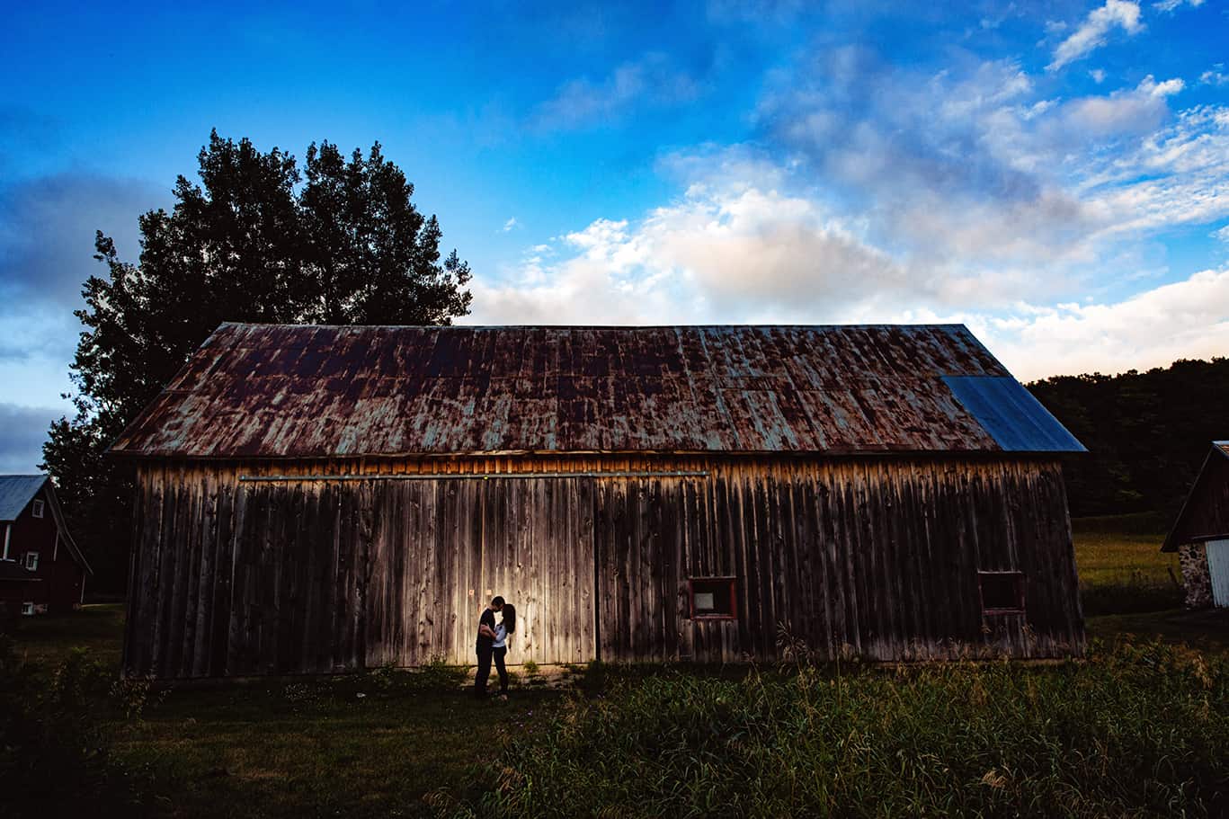 engagement photo in front of red barn with blue sky