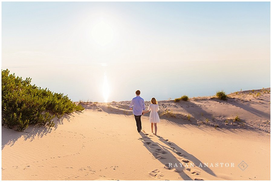 engagement photo of couple walking through sand dunes at sunset