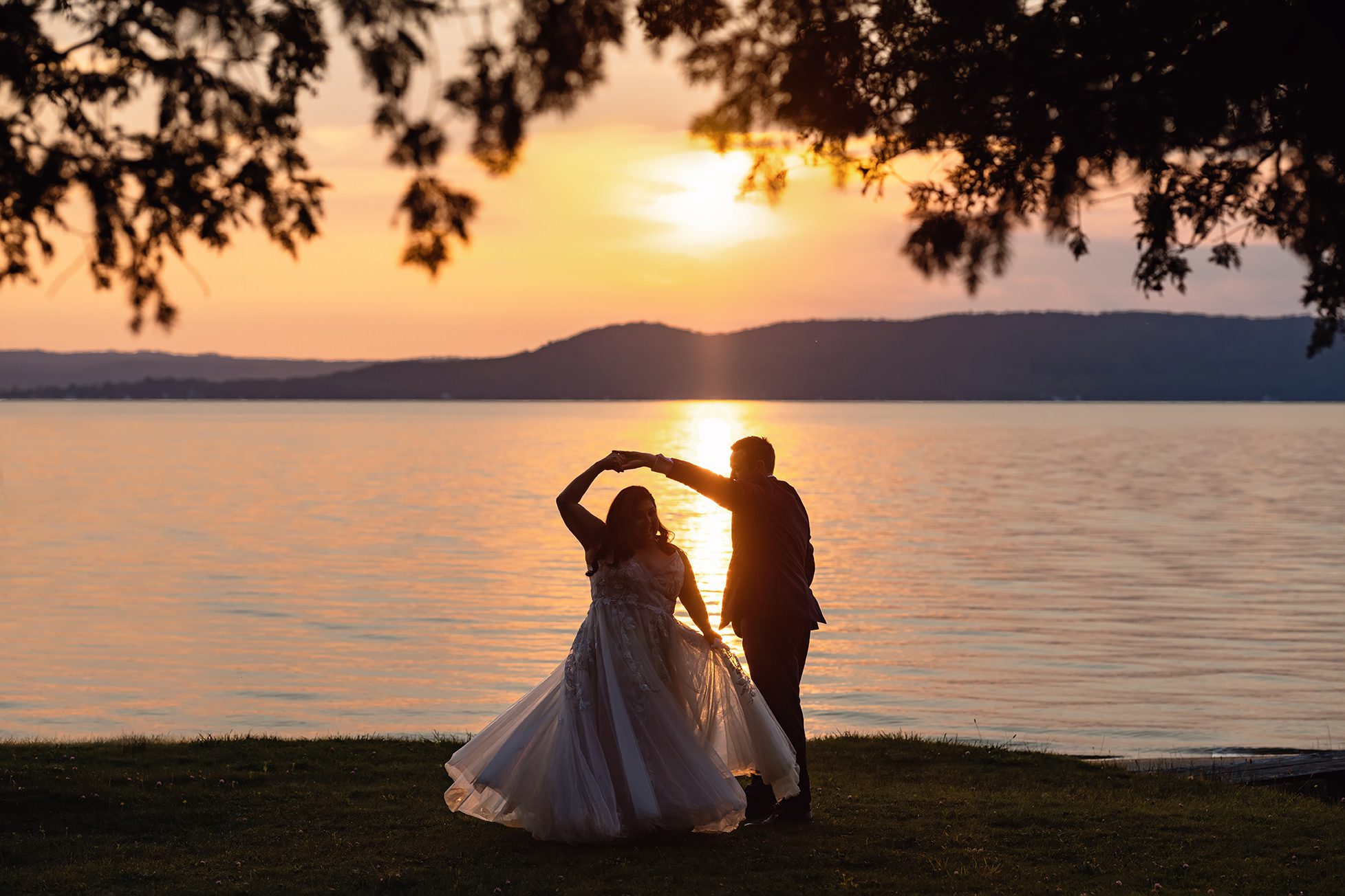 Bride and groom dancing by the lake at sunset