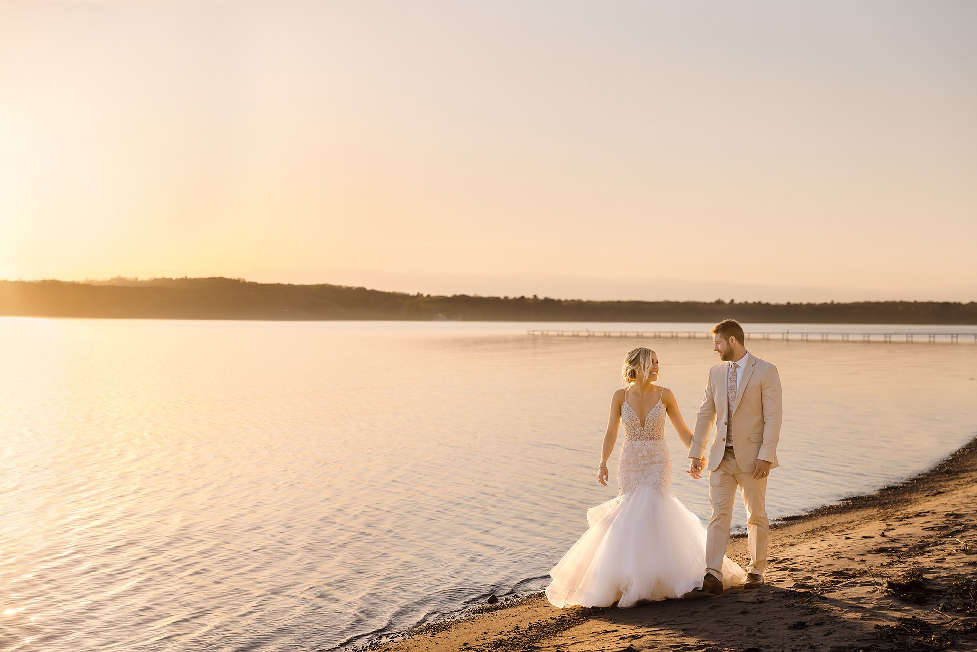 Bride and groom walking beach at sunset