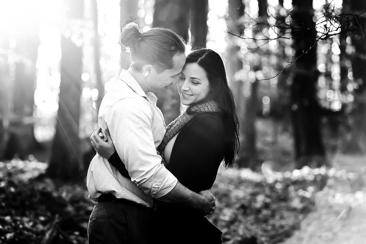 couple in woods for engagement photos with sun shining through
