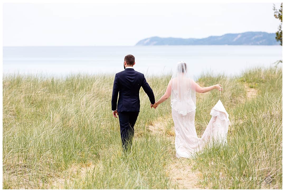 bride and groom walking through dune grass 