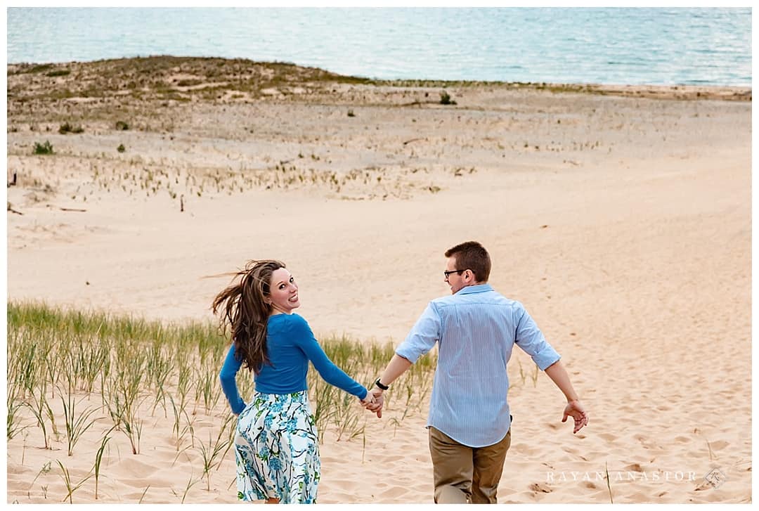 Couple running down sand dune for engagement photo session
