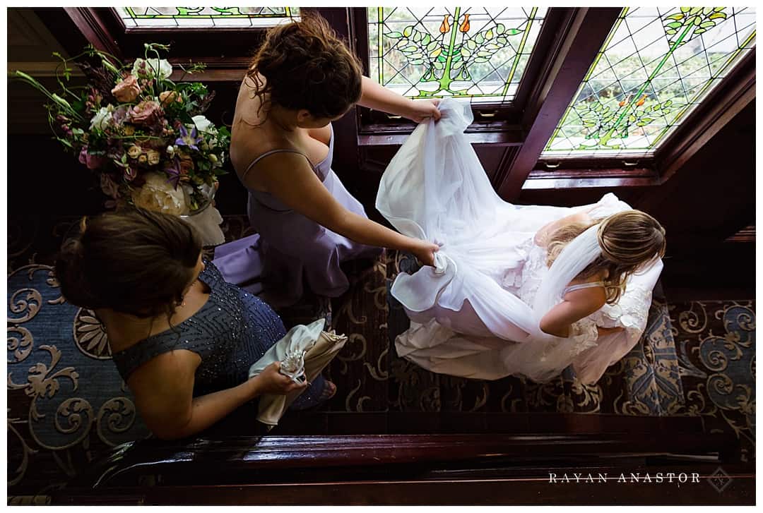 bride walking down stairs with bridesmaids holding her dress