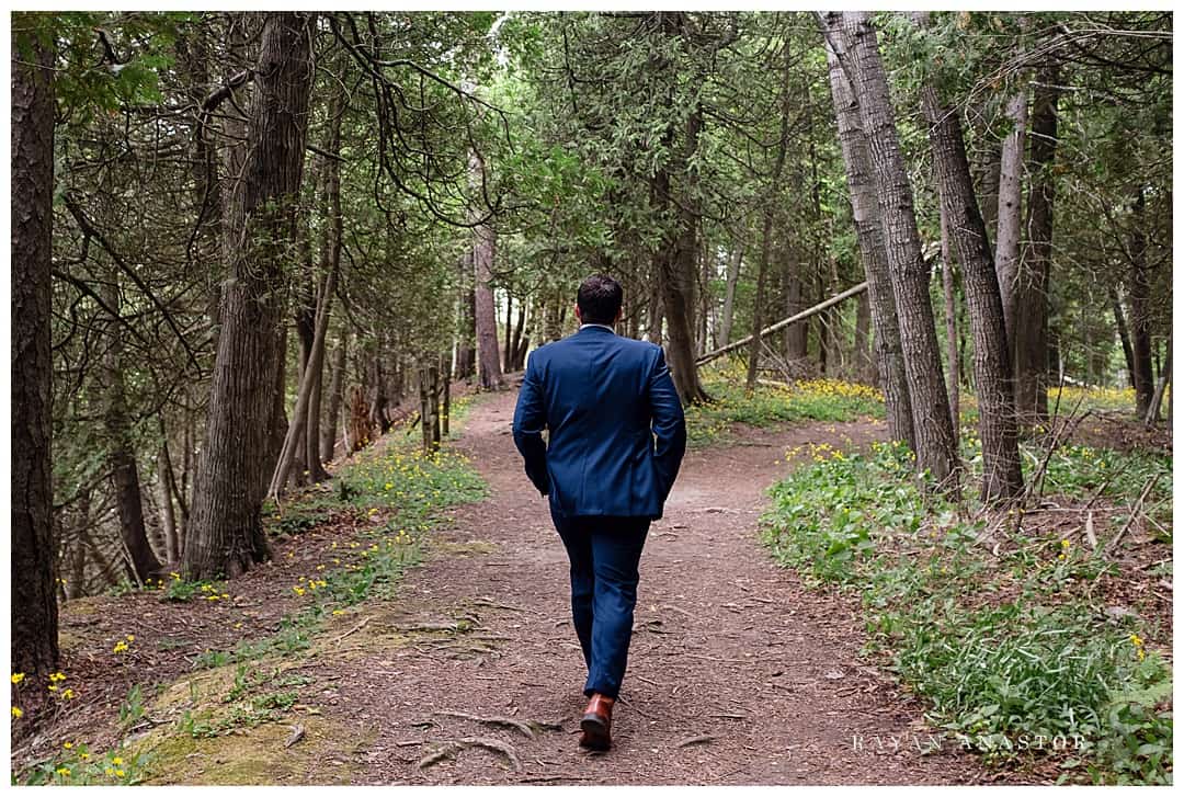 groom walking down tree lined path
