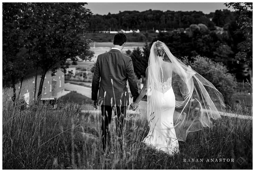 bride and groom walking through field with veil blowing