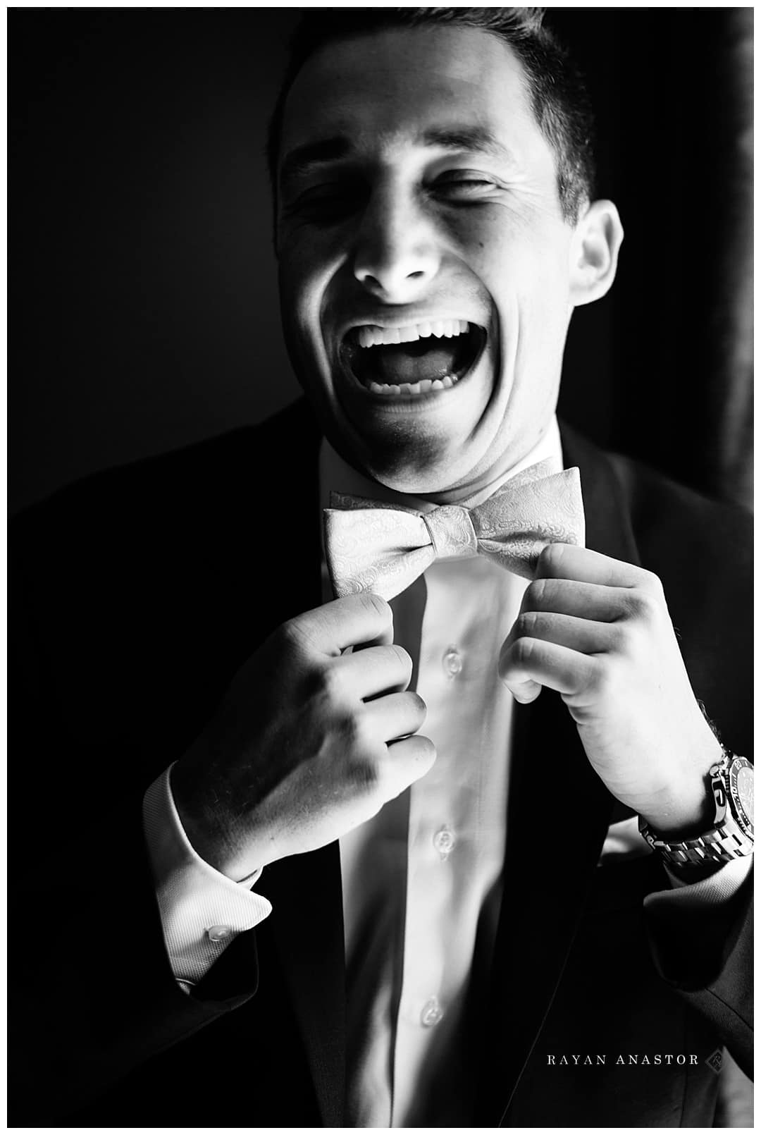 groom laughing at trying to tie bowtie